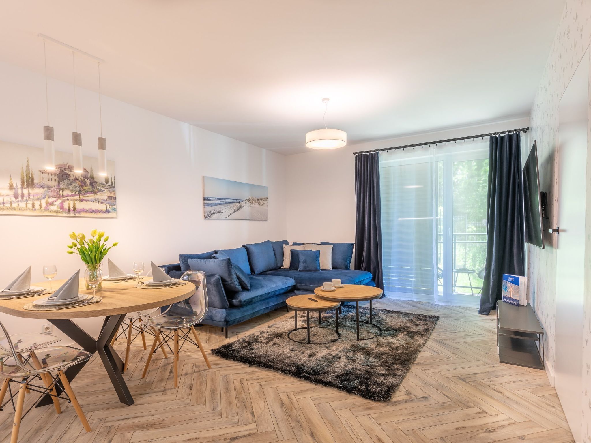 Una sala de estar moderna con un sofá azul, una mesa de comedor redonda y un amplio ventanal con cortinas.