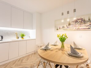 A modern kitchen with white cabinets, a wooden dining table set with white plates and a vase of yellow tulips, and a painting of a village on the wall. - Matejki 5 am Yachthafen von Usedom by Interhome (Swinoujscie)