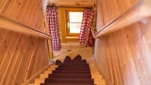 Eine Holztreppe mit Teppichhandlauf, die zu einer Tür mit karierten Vorhängen führt.