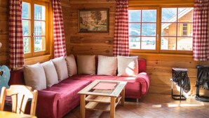 Ein gemütliches Blockhaus-Interieur mit Holzausstattung, einer Couch, einem Tisch und einem Fenster mit Vorhängen.