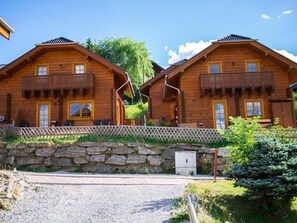 A wooden cabin with a stone wall entrance, a balcony, and a small outdoor seating area. - Tschaneck by Interhome (Sankt Margarethen im Lungau)