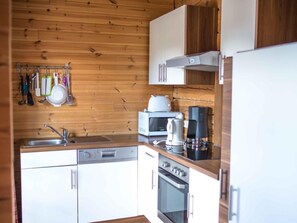 A compact kitchen with wooden walls, a built-in oven, a microwave, a coffee maker, and a sink. - Tschaneck by Interhome (Sankt Margarethen im Lungau)