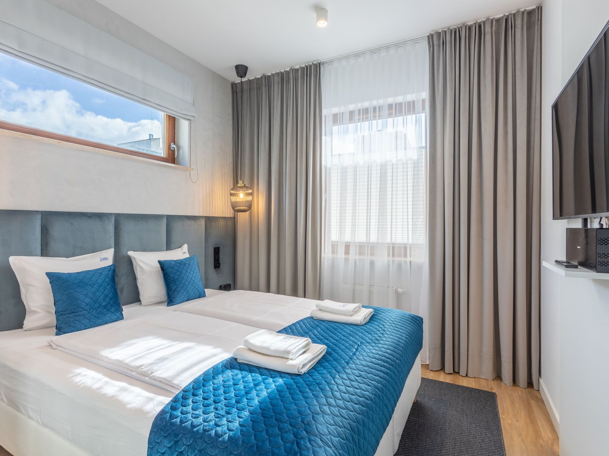 A hotel room with a large bed, a TV, and a window with curtains.