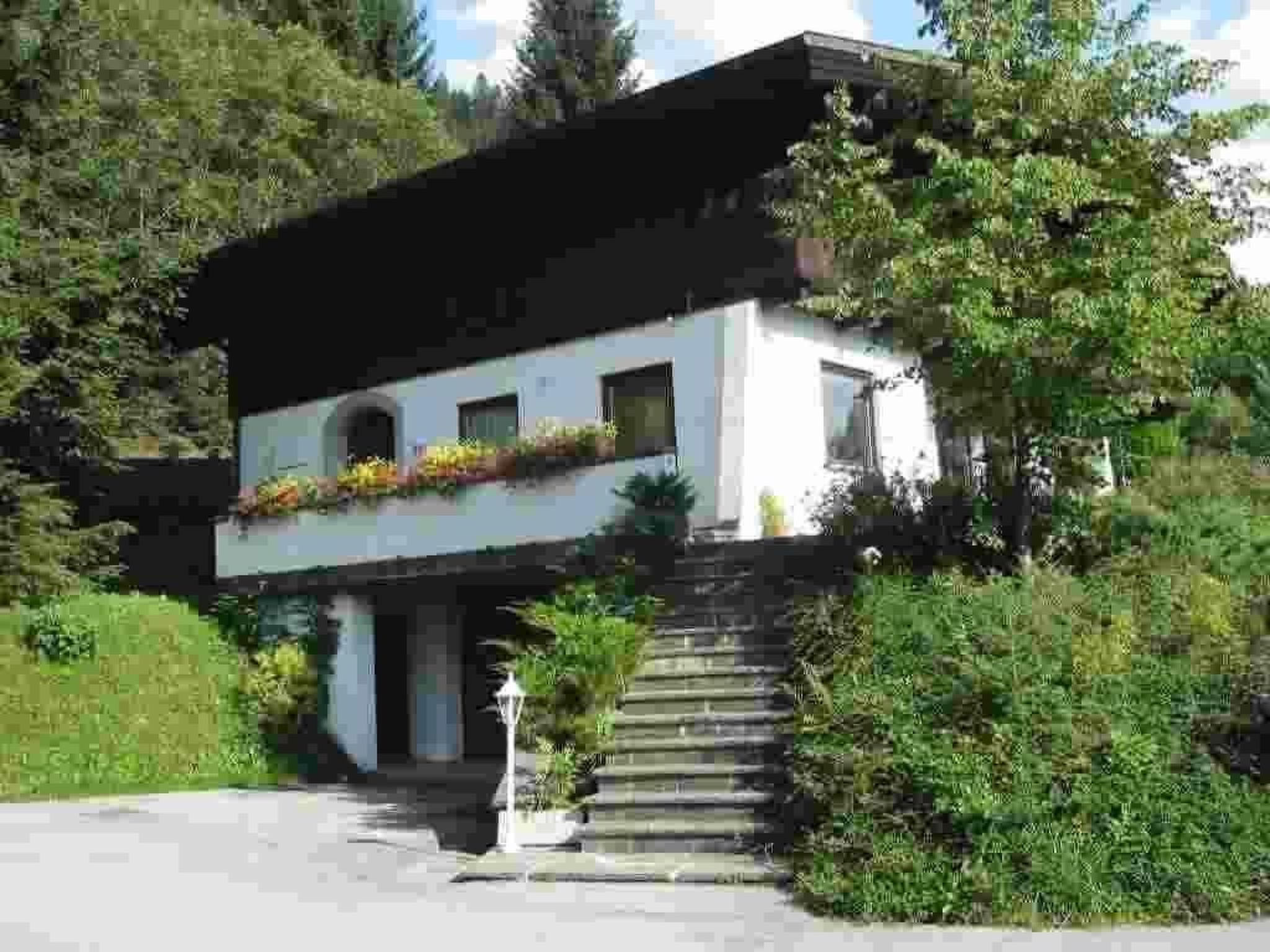 A modern two-story house with a sloped roof, a front entrance with steps, and a small garden area with flowers.