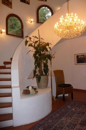 Una escalera con pared blanca, un candelabro, una planta en maceta, una silla y una alfombra estampada.