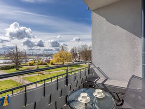 Ein Balkon mit Glastisch, zwei weißen Tassen und Blick auf einen Park und einen Fluss.