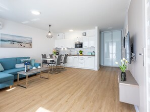 Ein modernes Wohnzimmer mit einem blauen Sofa, einem Esstisch mit Stühlen und einer Küchenzeile mit weißen Schränken und einer Mikrowelle.