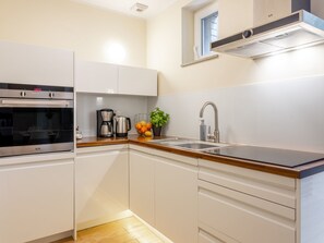 Eine moderne Küche mit weißen Schränken, einem Edelstahlbackofen, einer Kaffeemaschine und einem Waschbecken mit Armatur.