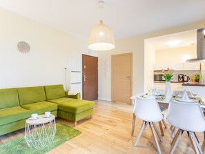 Ein modernes Wohnzimmer mit einem grünen Sofa, einem Esstisch für vier Personen und einer Küche im Hintergrund.