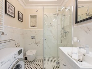 Une salle de bain moderne dotée d’une douche à parois de verre, d’un lave-linge et de toilettes.