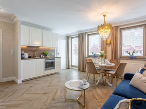 A modern kitchen with white cabinets, a dining area with a round table, and a blue sofa. - Rose 1 in Swinemünde am Meer by Interhome (Swinoujscie)