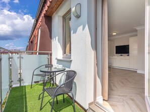 Un appartement moderne doté d’un balcon, d’un coin repas avec chaises et table, et d’une cuisine équipée de placards et d’un téléviseur.