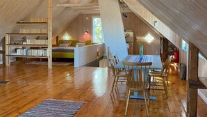 Een ruime zolderkamer met houten balken, een bed, een bureau en een eethoek met stoelen.