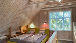 Een slaapkamer in loftstijl met een schuine kap, een groot raam, een bed met een geel hoofdeinde en een dakraam.