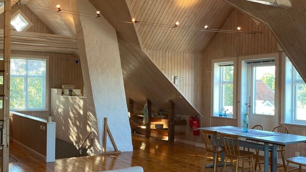 Een ruime loft met hoge plafonds, houten balken, een eethoek met een lange tafel en een gezellige zithoek met een bank en salontafel.