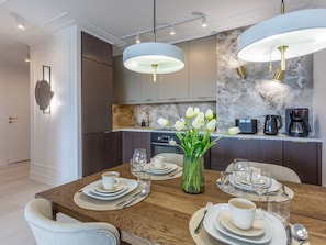 A modern dining area with a wooden table set for four, a vase of white flowers, and a kitchen in the background with marble backsplash and modern appliances. - Ruhige Ferienwohnung am Meer by Interhome (Swinoujscie)