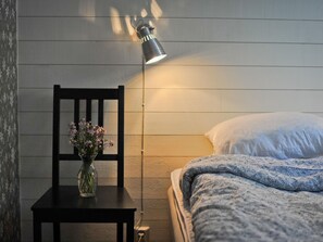 Een slaapkamer met een bed, een nachtkastje met een bloevas, een stoel en een vloerlamp.