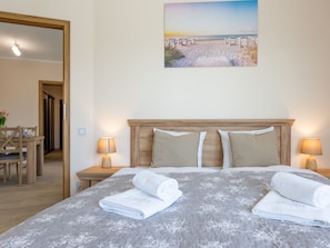 A hotel room with a bed, two nightstands, a lamp, a painting of a beach, and a wooden door. - Zentrum an der Ostsee by Interhome (Swinoujscie)