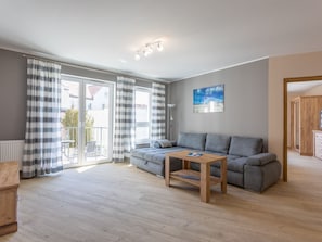 A modern living room with a grey sofa, a wooden coffee table, and a view of the outside through large windows with striped curtains. - Zentrum an der Ostsee by Interhome (Swinoujscie)