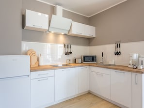 A modern kitchen with white cabinets, a wooden countertop, a built-in microwave, a coffee maker, and various utensils. - Zentrum an der Ostsee by Interhome (Swinoujscie)