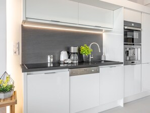A modern kitchen with a black countertop, white cabinets, a coffee maker, a sink, and a built-in oven. - Helle Ferienwohnung Tower 76 auf Usedom by Interhome (Swinoujscie)