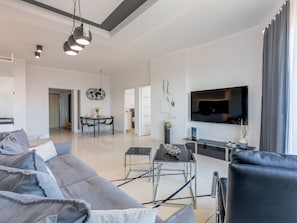 A modern living room with a grey sofa, a coffee table, and a TV. There is a dining area with a table and chairs in the background. - Helle Ferienwohnung Tower 76 auf Usedom by Interhome (Swinoujscie)