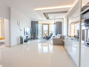 Een moderne woonkamer met een bank, een eethoek en een keuken met roestvrijstalen apparatuur.