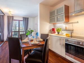 A modern kitchen with a dining area, featuring a wooden table set for four, a built-in oven, and a large window with curtains. - Urlaub auf Usedom, Apartment Wind Rose 33 by Interhome (Swinoujscie)
