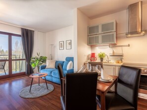 A modern living room with a blue sofa, dining table, and chairs. There is a kitchen area with cabinets and a coffee machine. - Urlaub auf Usedom, Apartment Wind Rose 33 by Interhome (Swinoujscie)