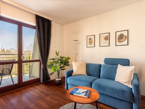 A modern living room with a blue sofa, a coffee table with a book, a potted plant, and a balcony with a view. - Urlaub auf Usedom, Apartment Wind Rose 33 by Interhome (Swinoujscie)