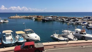 A marina with various boats docked, a rocky breakwater, and a clear blue sky. - "Palmenvilla" mit privatem Balkon by Interhome (Agios Georgios Pegeias)