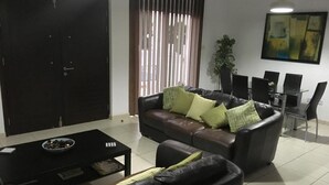 A living room with a sofa, coffee table, and a dining area with chairs and a table. - "Palmenvilla" mit privatem Balkon by Interhome (Agios Georgios Pegeias)