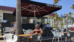 An outdoor seating area with tables and chairs, a Costa Coffee sign, and a barista in uniform. - "Palmenvilla" mit privatem Balkon by Interhome (Agios Georgios Pegeias)