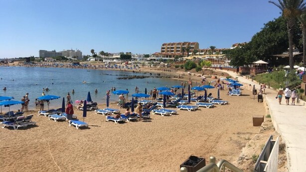 A beach with sun loungers and umbrellas, a clear sky, and buildings in the background. - "Palmenvilla" mit privatem Balkon by Interhome (Agios Georgios Pegeias)