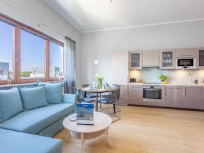 Ein modernes Wohnzimmer mit einer Couch, einem Esstisch und einer Küchenzeile mit Schränken und Geräten.