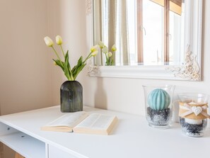 Ein weißer Schreibtisch mit einem offenen Buch, einer Vase mit Tulpen und dekorativen Glasbehältern.