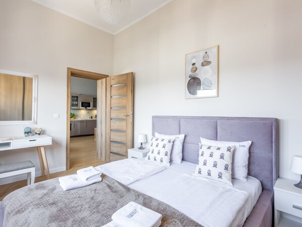Una camera da letto moderna con un letto grande, un comodino, una scrivania e un bagno visibile attraverso una porta aperta.