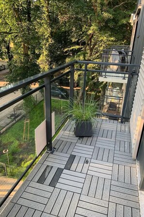 A wooden deck with a metal railing, a potted plant, and a view of trees and a car in the background. - am Meer, Urlaub auf der Insel Usedom, Apartment Matejki 27 by Interhome (Swinoujscie)