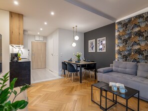 A modern living room with a grey sofa, a dining table with chairs, a coffee table, and a kitchen area with a coffee machine. - am Meer, Urlaub auf der Insel Usedom, Apartment Matejki 27 by Interhome (Swinoujscie)