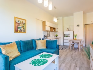 A modern living room with a teal sofa, a white coffee table with green leaf designs, a kitchen in the background, and a dining area with a wooden table and chairs. - Tower 22 in ruhigem Stadtviertel by Interhome (Swinoujscie)