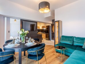 A modern living room with a teal sofa, a dining area with a round table and chairs, and a kitchen in the background. - Appartement Tower 65 in einem ruhigen Stadtviertel by Interhome (Swinoujscie)
