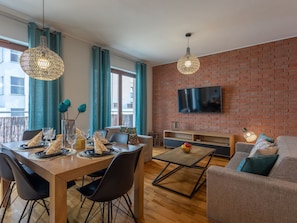 Ein modernes Wohnzimmer mit Essbereich, einer Ziegelwand, einem Flachbildfernseher und einem Balkon mit Vorhängen.