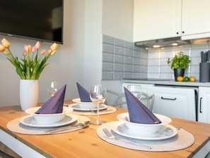 A modern kitchen with white cabinets, a tiled backsplash, and a wooden countertop. There are three white plates with purple napkins, a glass of white wine, and a vase with tulips on the counter. - Ferienappartement Blue Rose direkt am Park by Interhome (Swinoujscie)