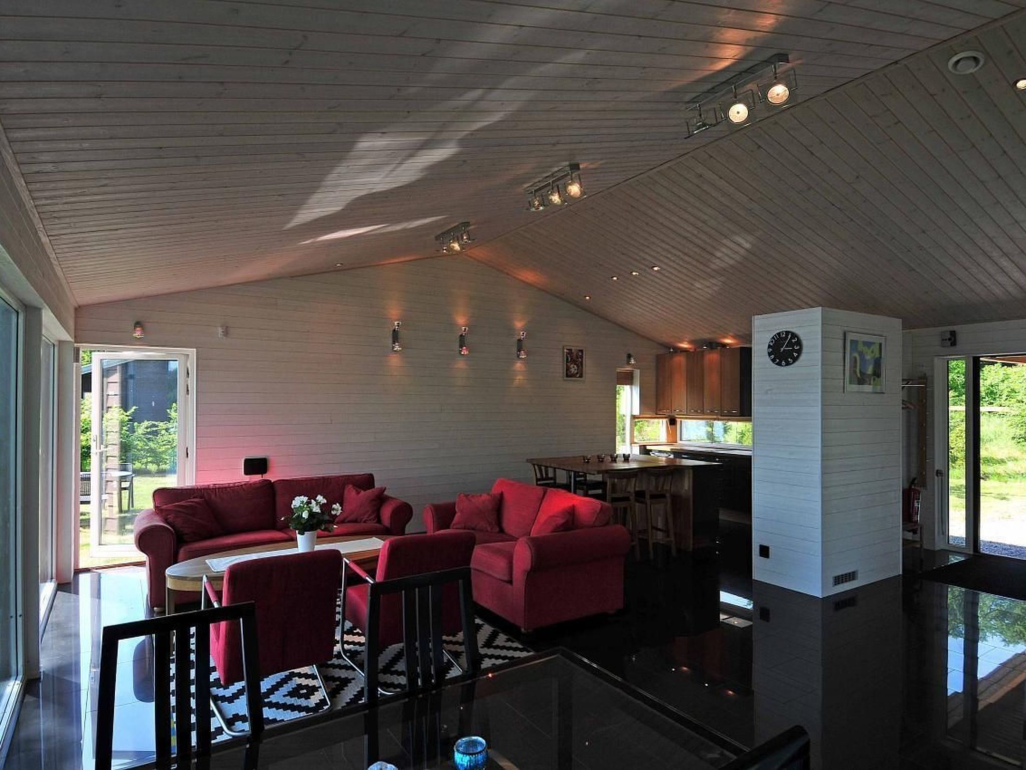 A spacious living area with red sofas, a glass coffee table, and a kitchen in the background.