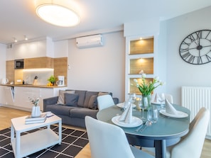 A modern kitchen with a microwave, coffee maker, and a plant on the counter. There is a dining area with a round table set for two, a sofa, and a clock on the wall. - Helle Ferienwohnung Albus direkt am Strand by Interhome (Swinoujscie)