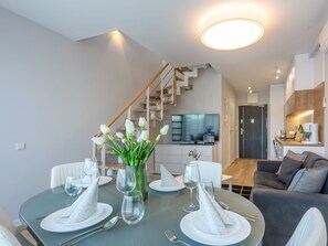 A modern dining area with a round table set for four, a vase of white flowers, and a staircase leading to a kitchen. - Helle Ferienwohnung Albus direkt am Strand by Interhome (Swinoujscie)