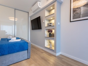 A modern hotel room with a bed, a flat-screen TV, built-in shelves with books and decorative items, and a large window. - Helle Ferienwohnung Albus direkt am Strand by Interhome (Swinoujscie)