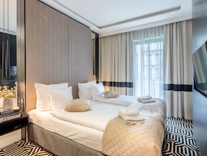 Et hotelværelse med en stor seng, et natbord med lampe, et fjernsyn og udsigt over byen gennem vinduet.