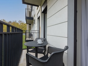 Ein Balkon mit rundem Tisch und zwei Stühlen, ein kleiner Tisch mit einer Tasse und ein Sessel mit einer Tasse.