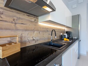 A modern kitchen with a wooden backsplash, stainless steel appliances, and a black countertop. - Urlaub auf Usedom - Ferienwohnung Tower 13 by Interhome (Swinoujscie)